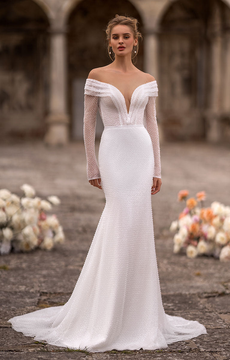 Woman wearing a white off-shoulder wedding dress in an outdoor setting with flowers.