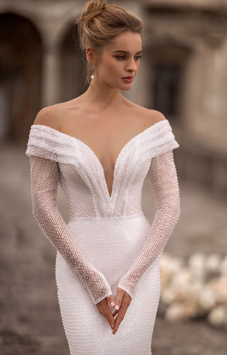 Woman wearing a white off-shoulder dress with long sleeves in an outdoor setting.