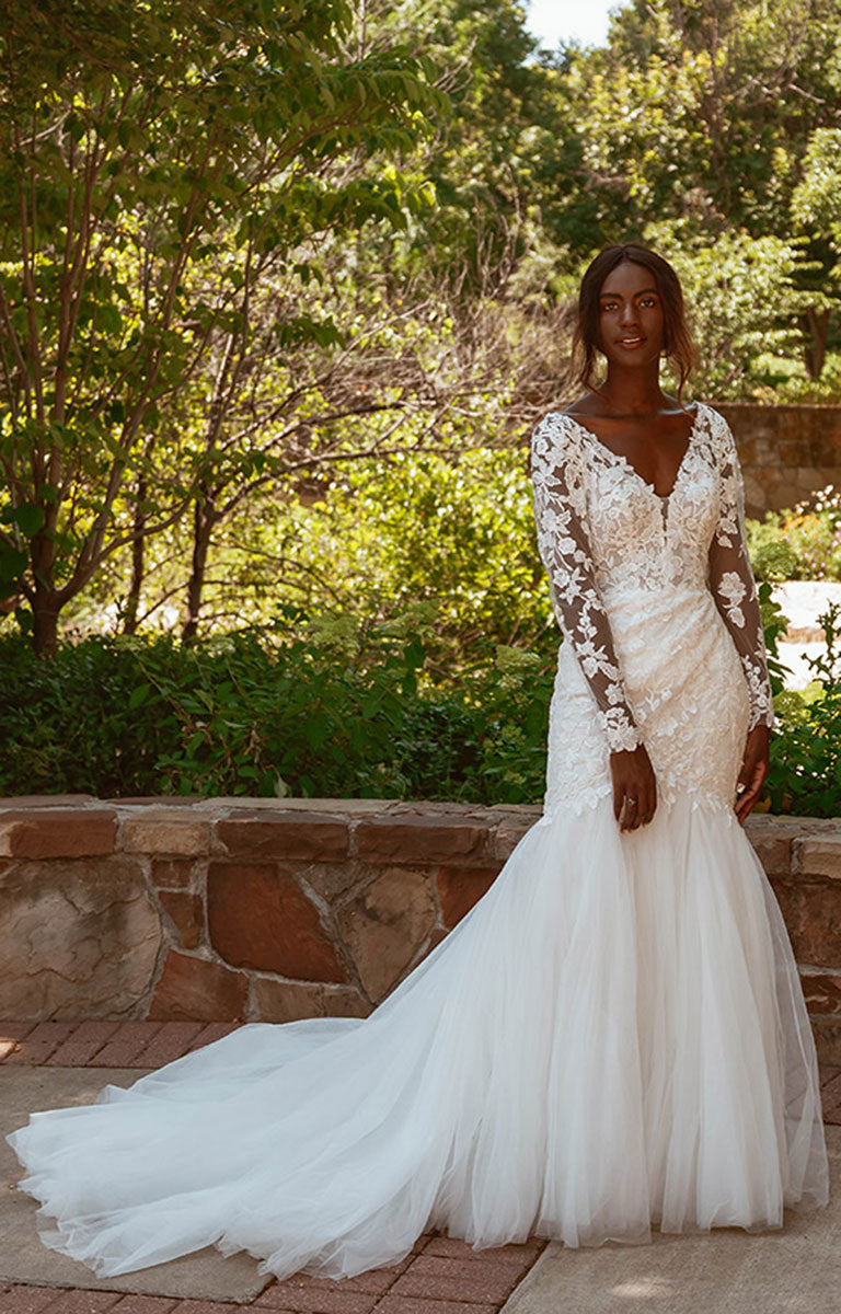 Woman in Style 7491 by Essense of Australia - Long Sleeve Lace Fit-and-Flare Wedding Dress with Train standing outdoors with greenery in the background