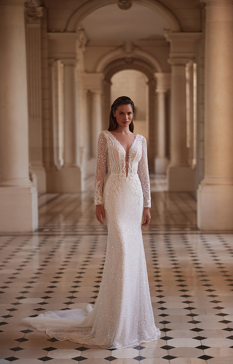 Woman in a white lace wedding dress standing in an elegant hallway with columns.
