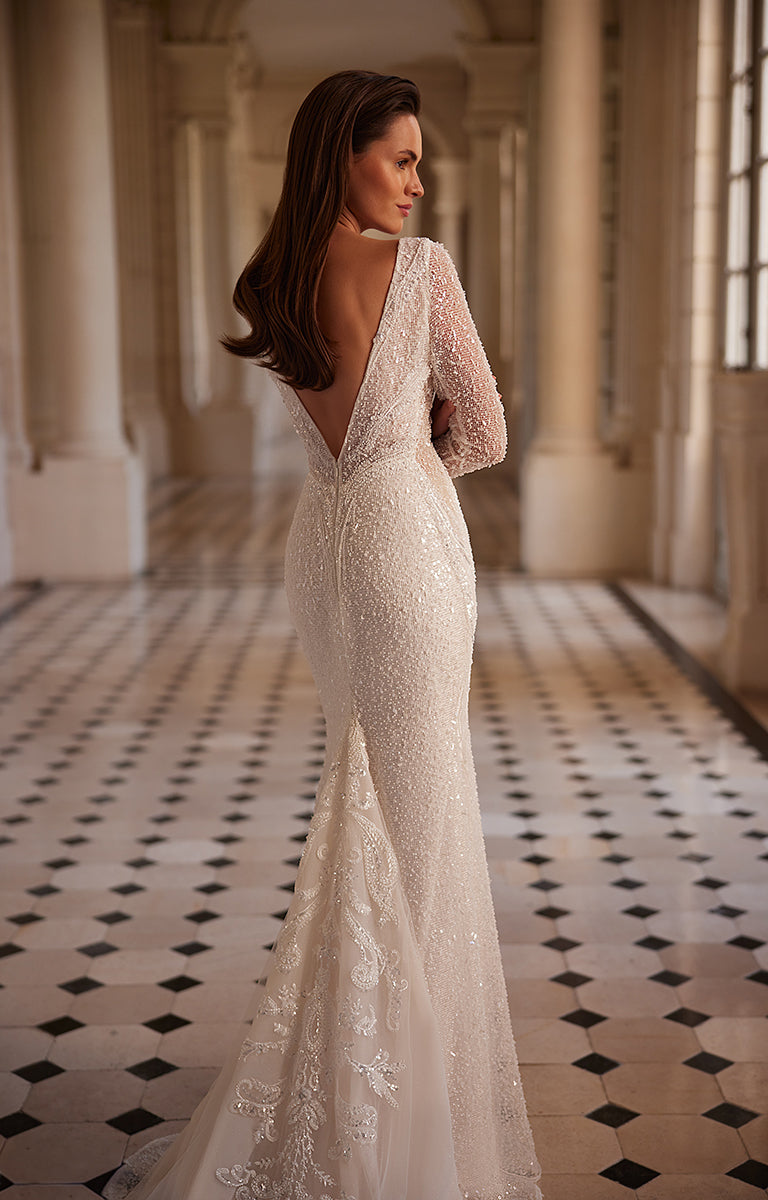Woman in a lace wedding dress standing in an elegant hallway with columns and tiled floor.