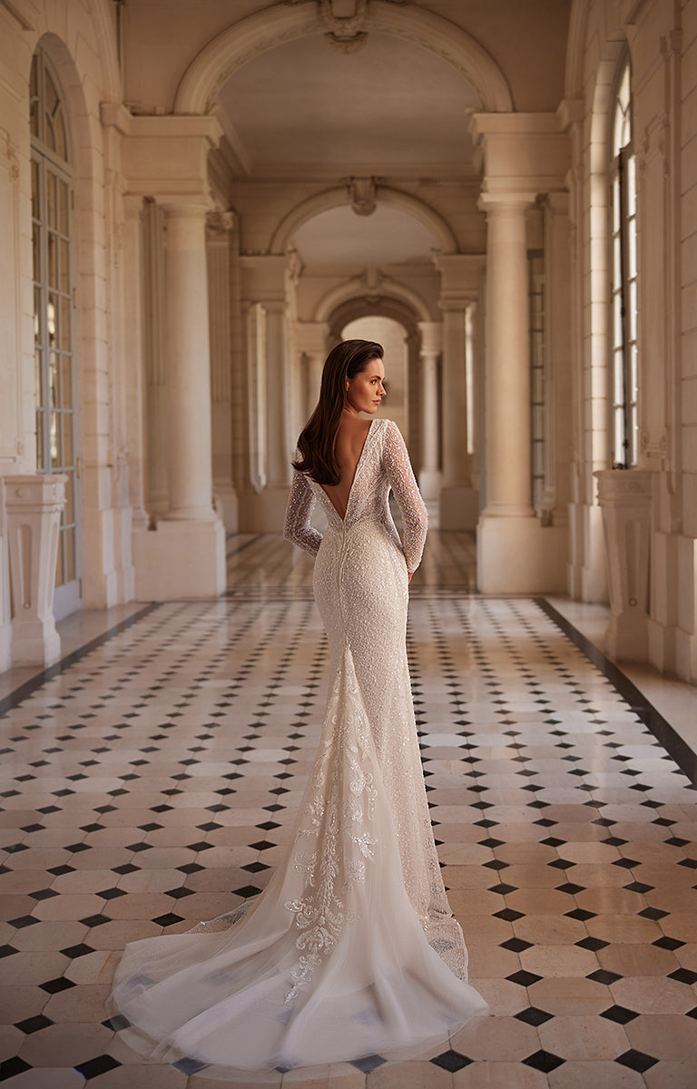 Woman in a white lace wedding dress standing in an elegant hallway with columns and a checkered floor.