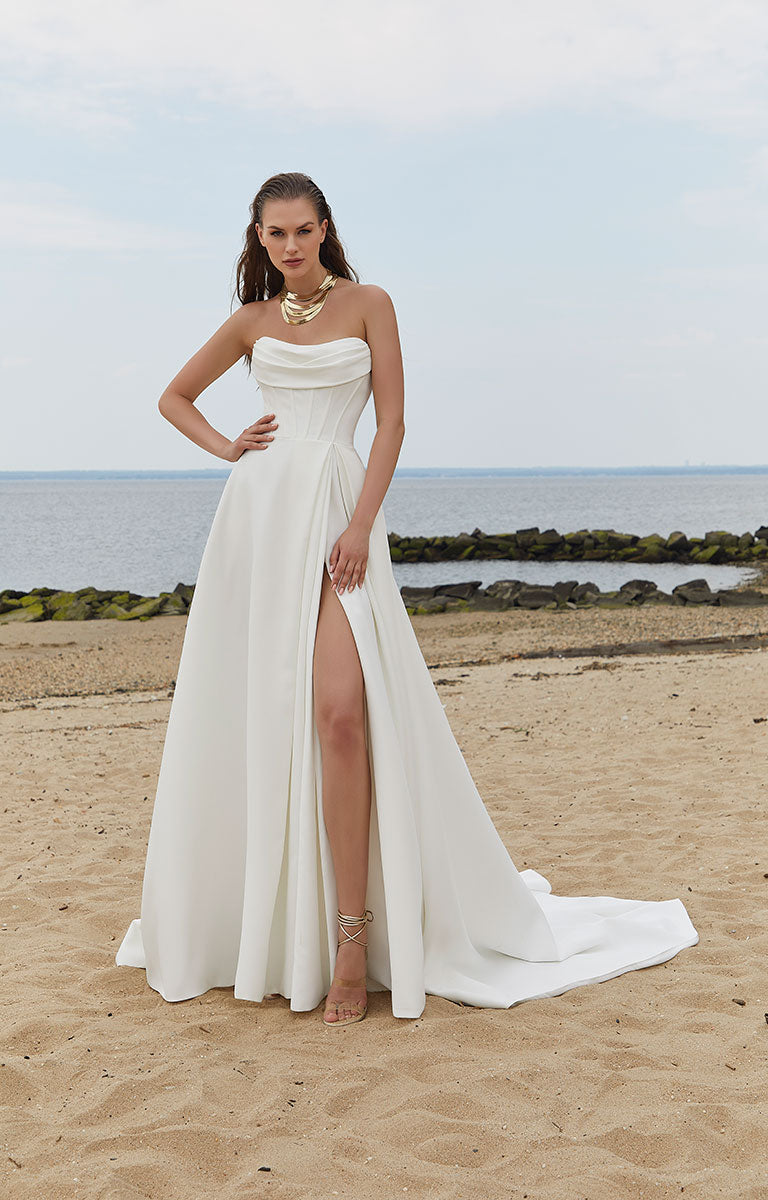 Woman in a strapless white gown with a high slit on a beach.