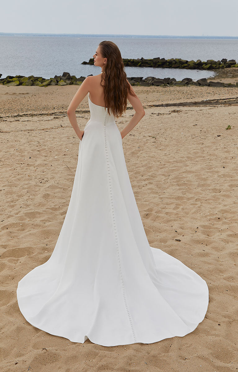 Woman in a white wedding dress standing on a beach with ocean and rocks in the background