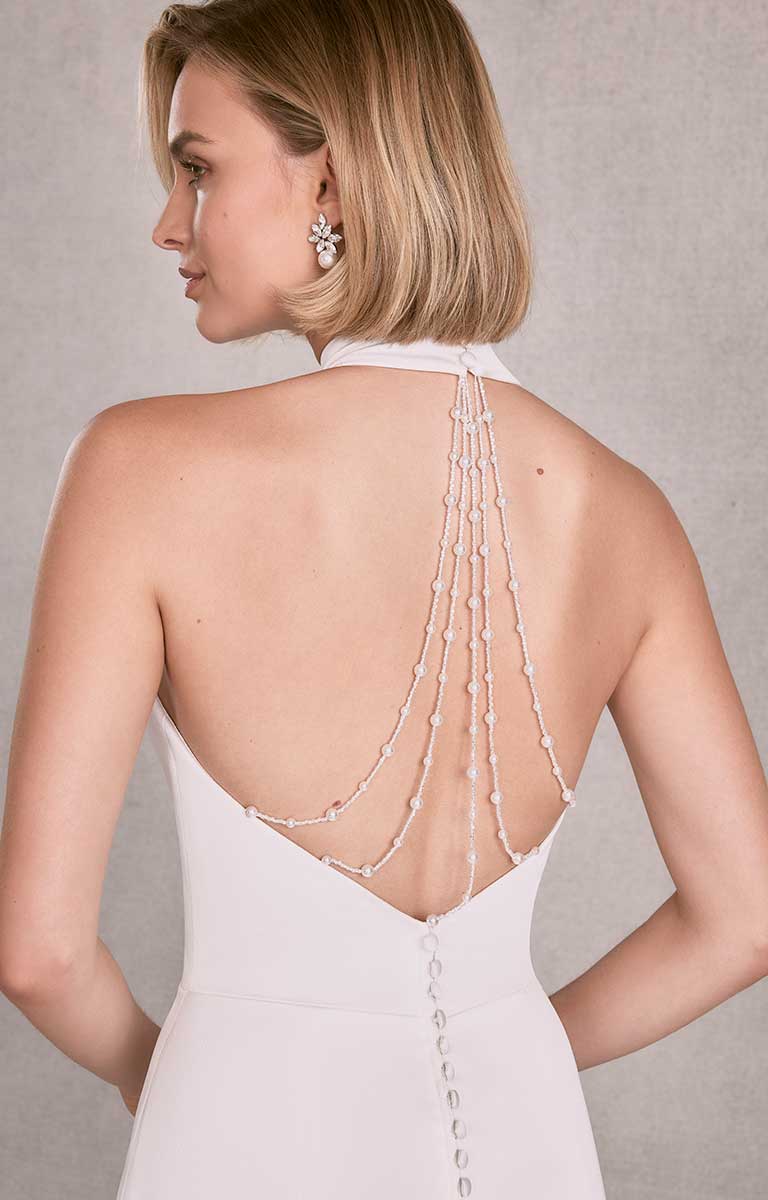 Woman wearing a white dress with a beaded back detail on a neutral background