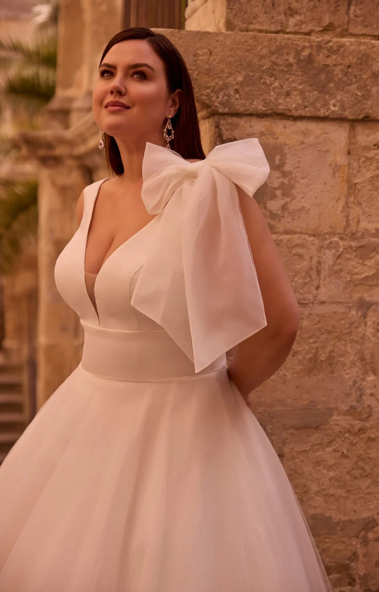 Woman wearing Yudita by Veni Infantino Bridal - Princess A-Line Ball Gown with Statement Bow Detail in front of a stone wall.