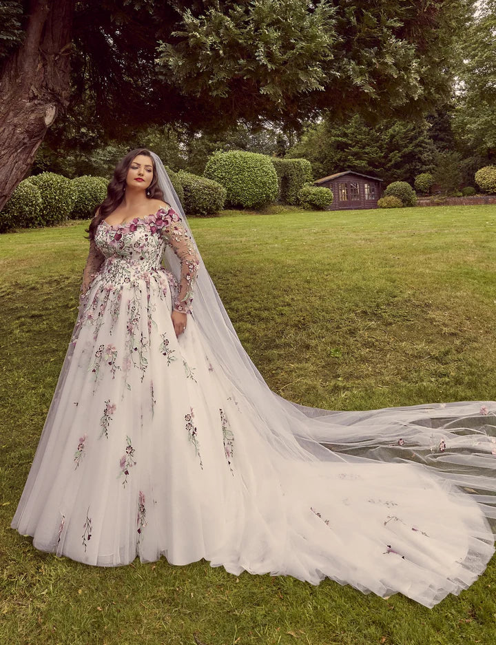 Woman in a white wedding dress with floral embroidery standing in a garden.