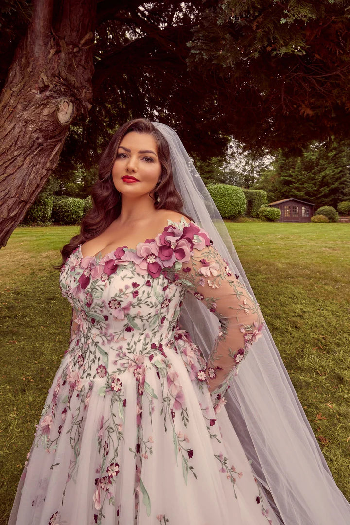 Woman in a floral wedding dress with a veil standing outdoors.