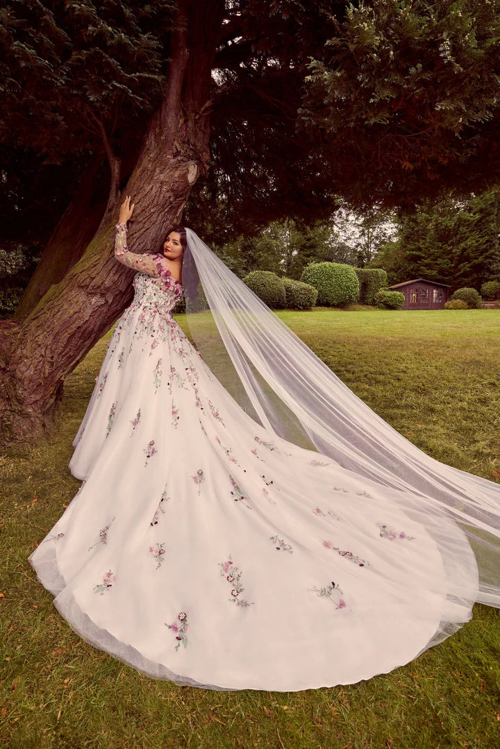 Woman in a white wedding dress with floral embroidery standing under a tree in a park.