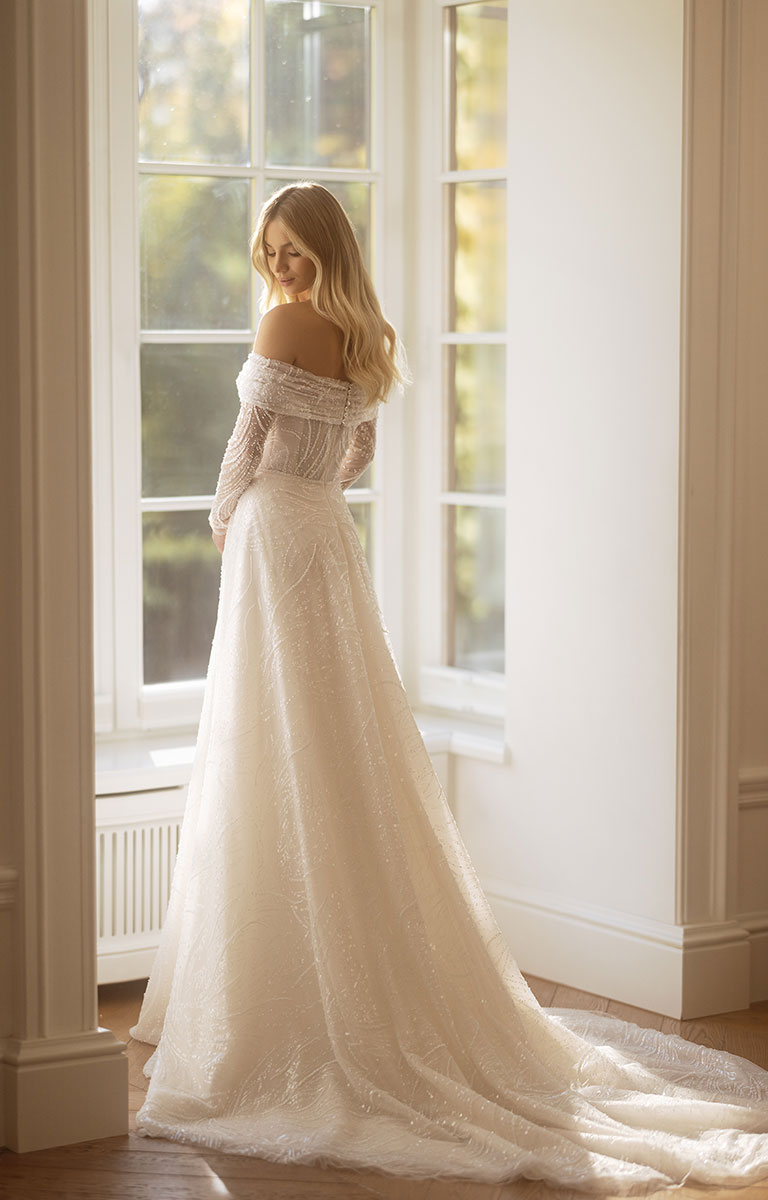 Woman in a white wedding dress standing in a room with large windows.