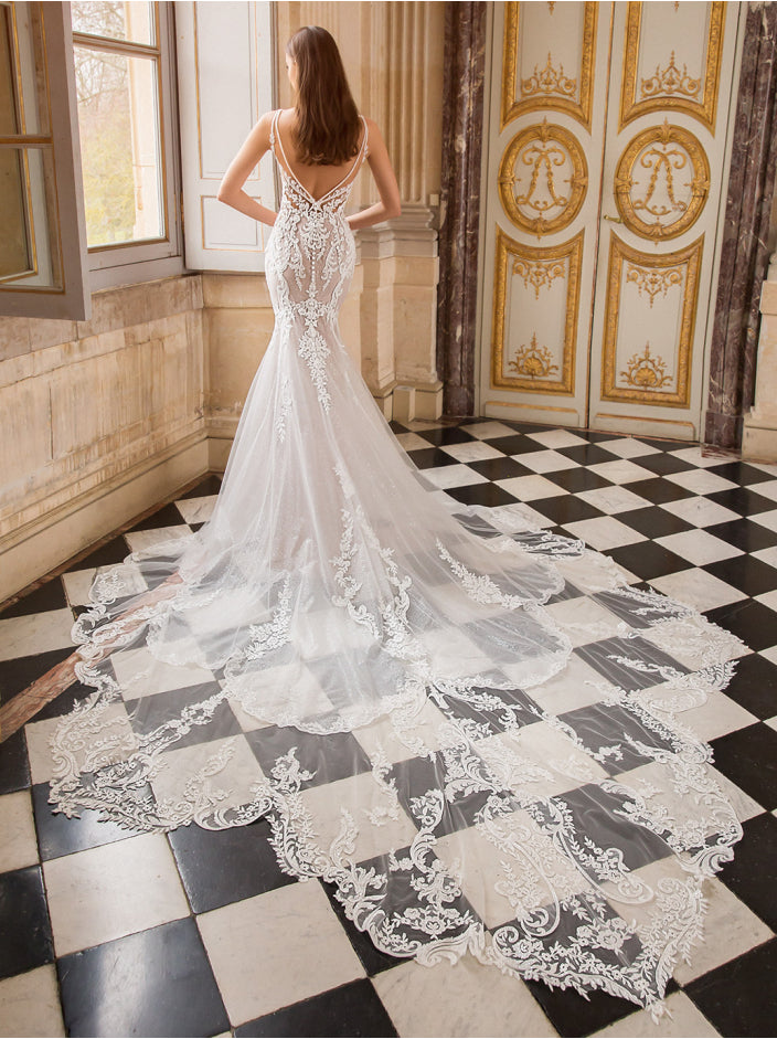Woman in a white lace wedding dress standing in an ornate room with checkered floor.
