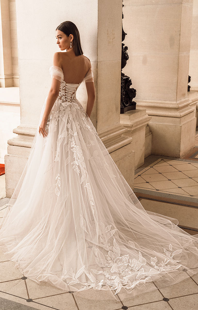 Woman in a white lace wedding dress standing in an elegant indoor setting.