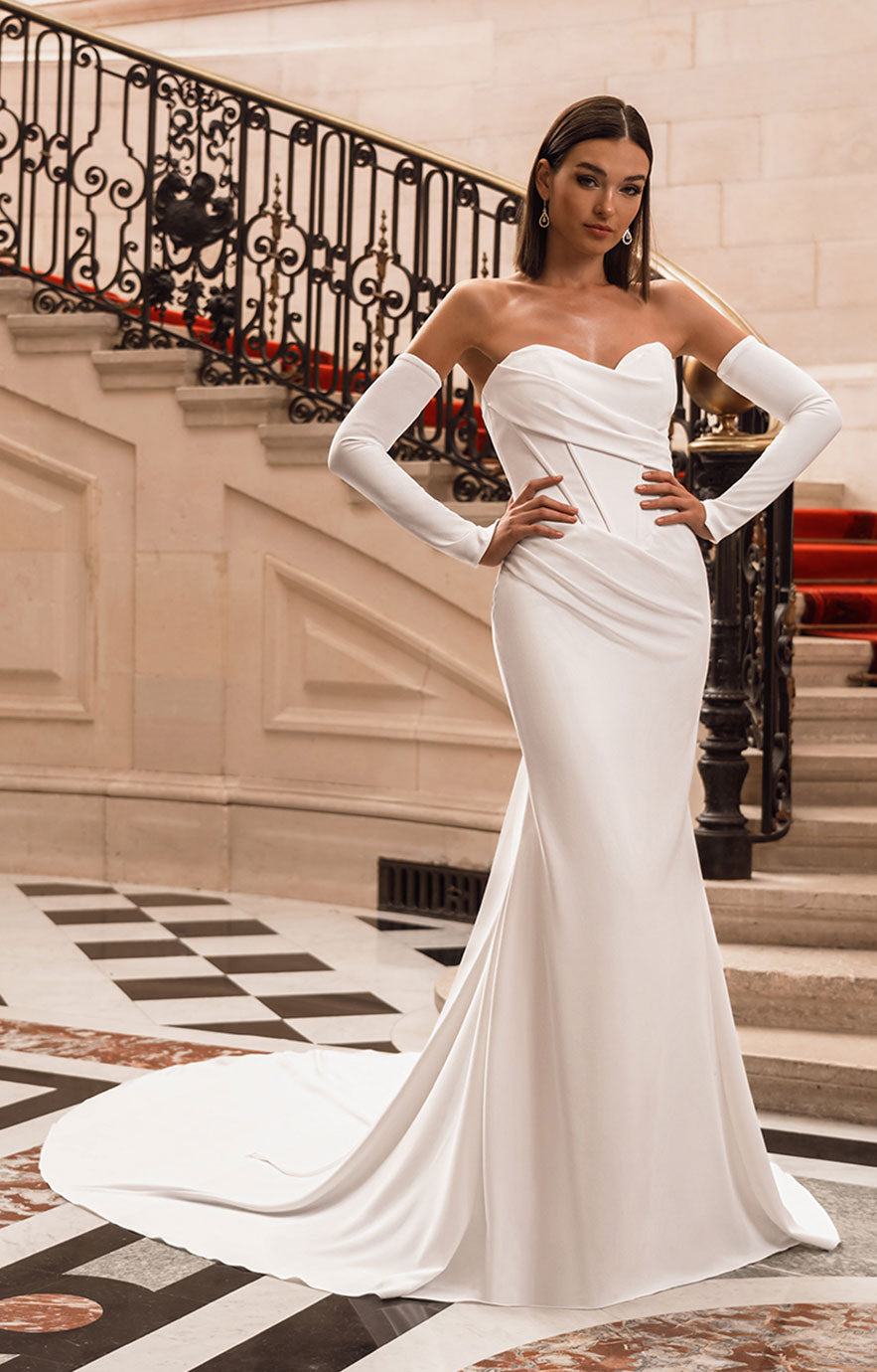 Woman in a white strapless gown with long sleeves standing in an elegant interior setting.