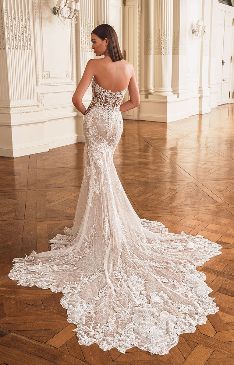 Woman in a white lace wedding dress standing in an elegant room with wooden floor and white walls.