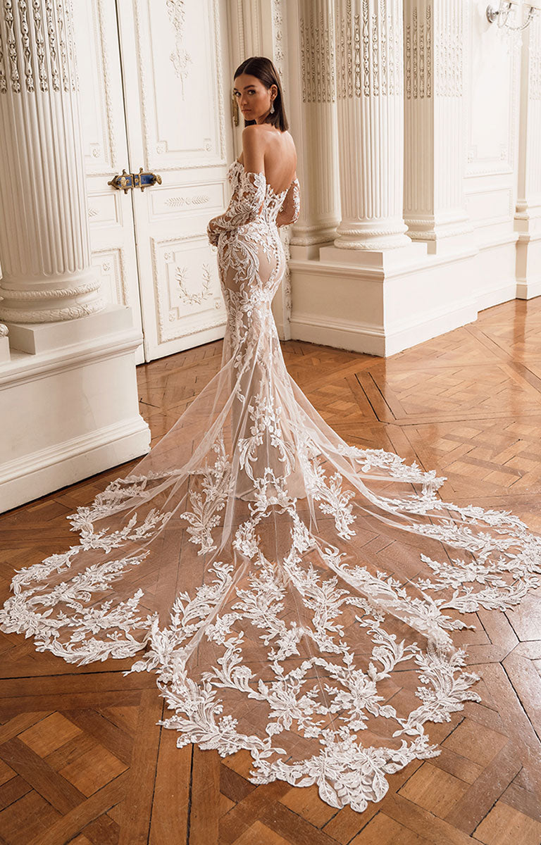 Woman in a white lace wedding dress standing in an elegant room with columns.