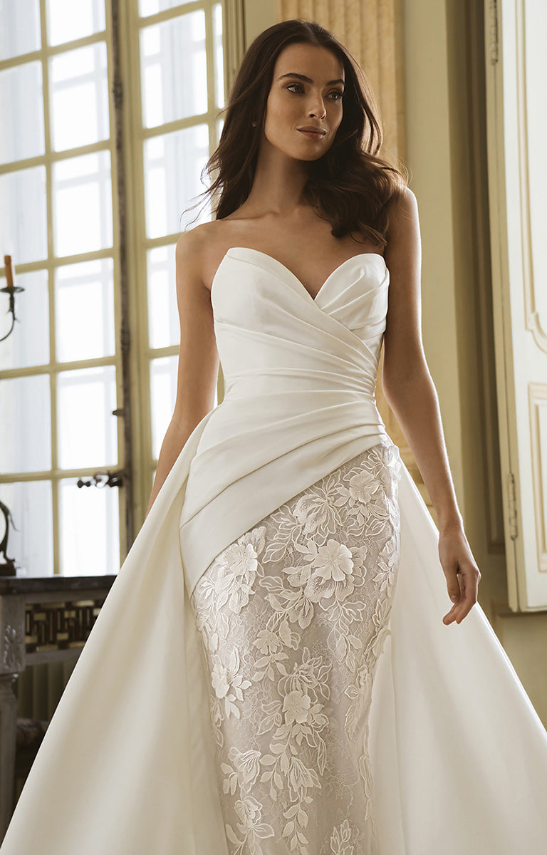 Woman wearing a strapless wedding dress with lace detailing in a softly lit room.