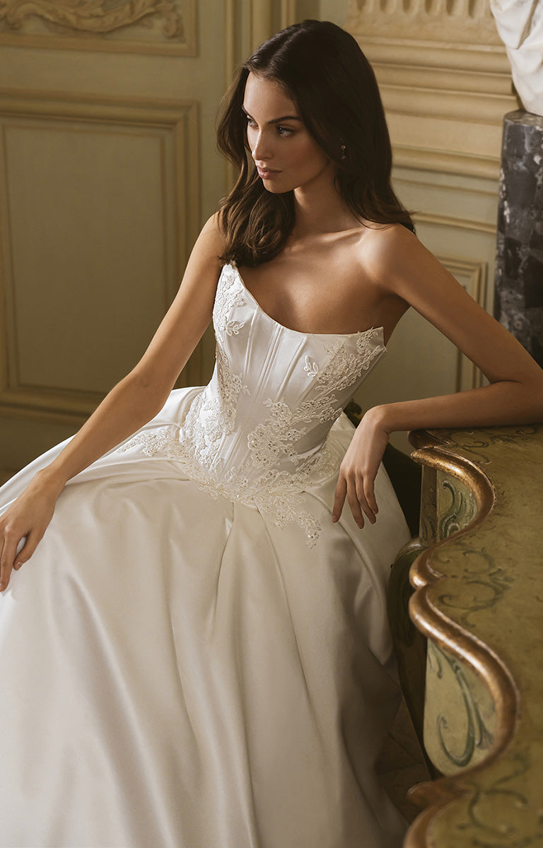 Woman in a white wedding dress sitting on an ornate chair in a elegant room.