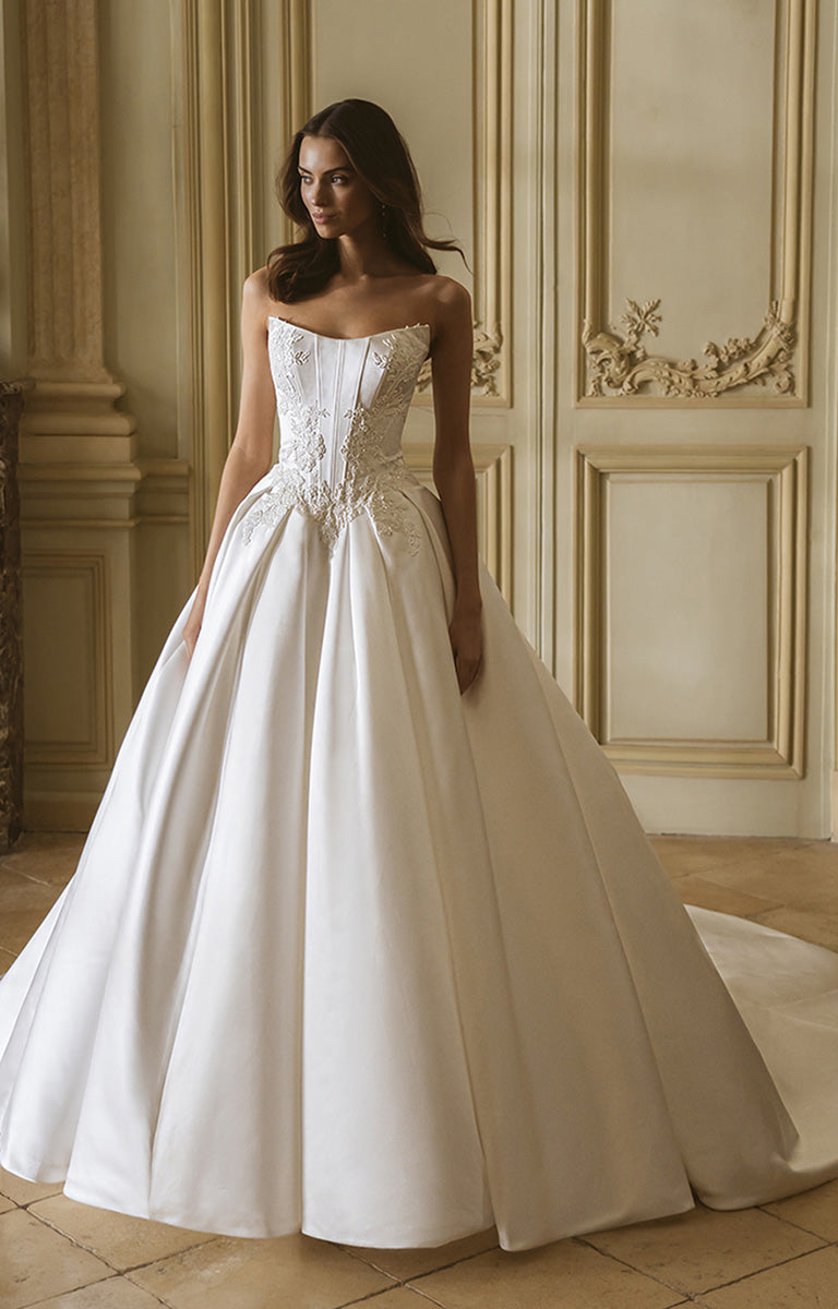 Woman in a white wedding dress standing in an elegant room with ornate walls.