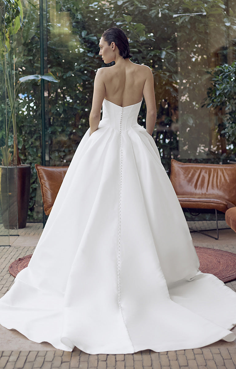 Woman wearing a white wedding dress with an open back, standing outdoors.