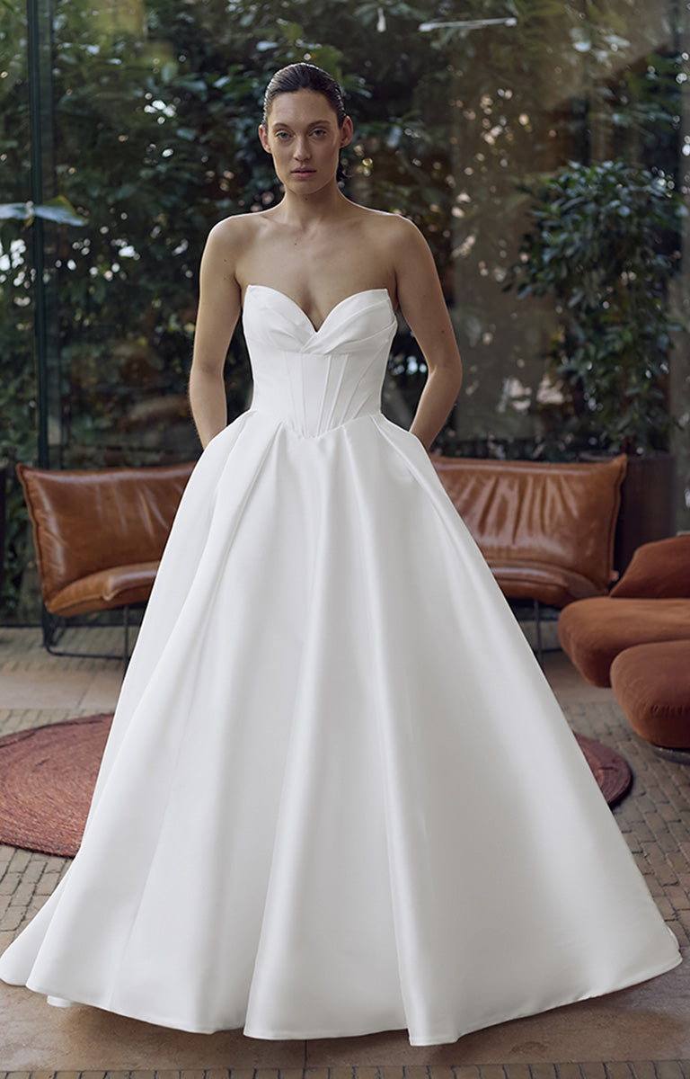 Woman wearing a white strapless gown in an outdoor setting with greenery and brown furniture.