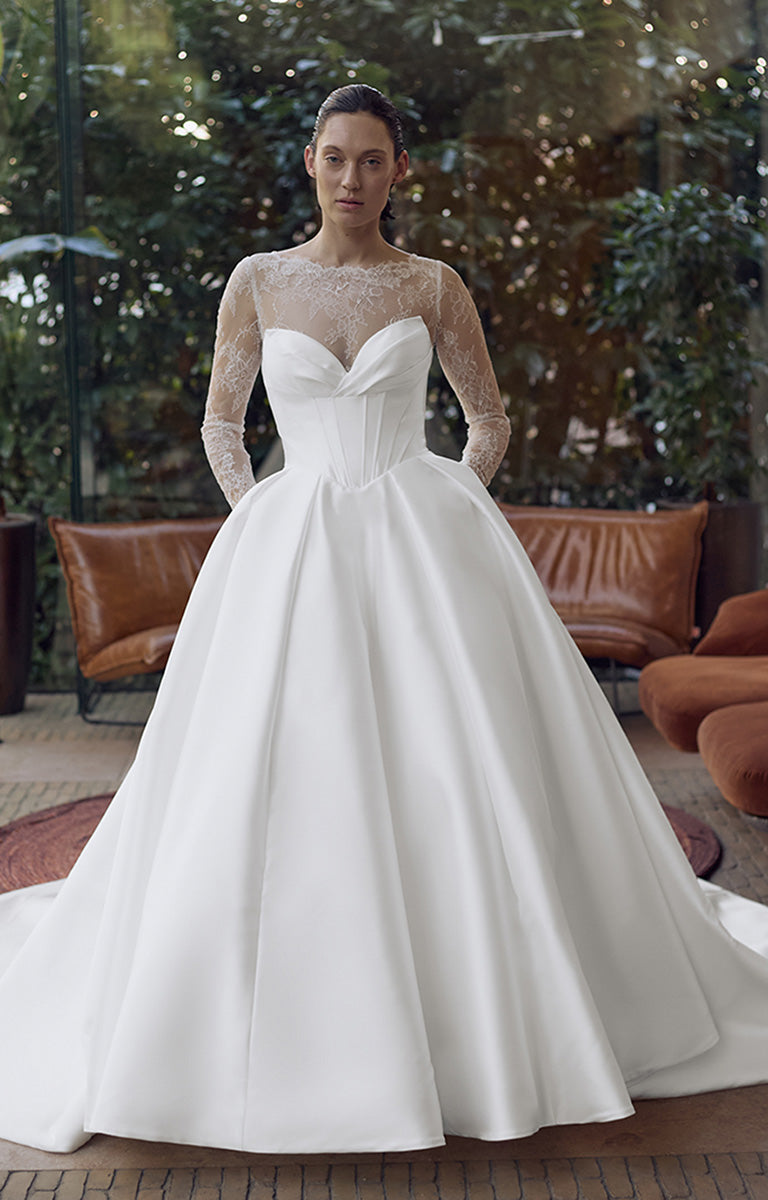 Woman wearing a white wedding dress with sheer sleeves in an outdoor setting.