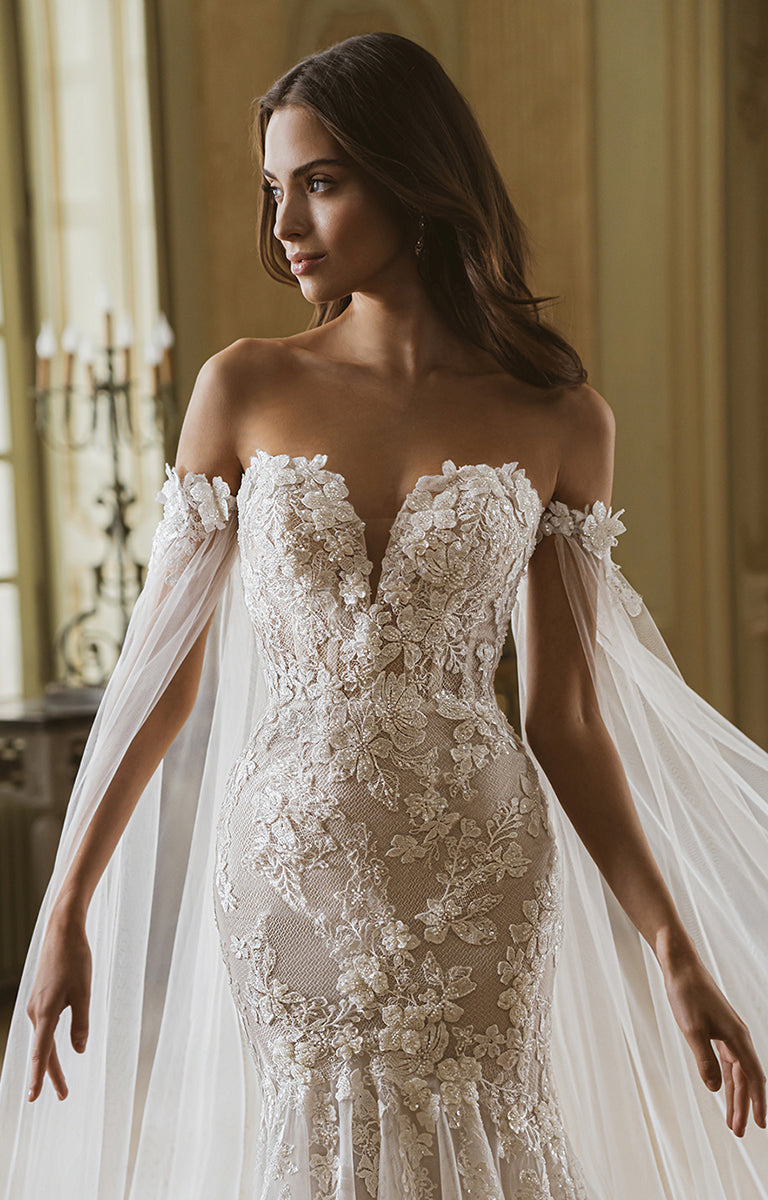 Woman wearing a white lace wedding dress with a flowing train indoors.