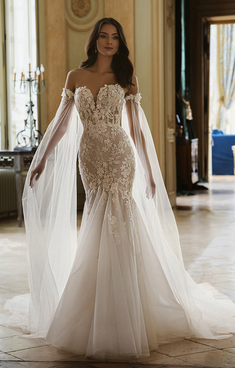 Woman wearing a white wedding dress with floral lace details in an elegant indoor setting.