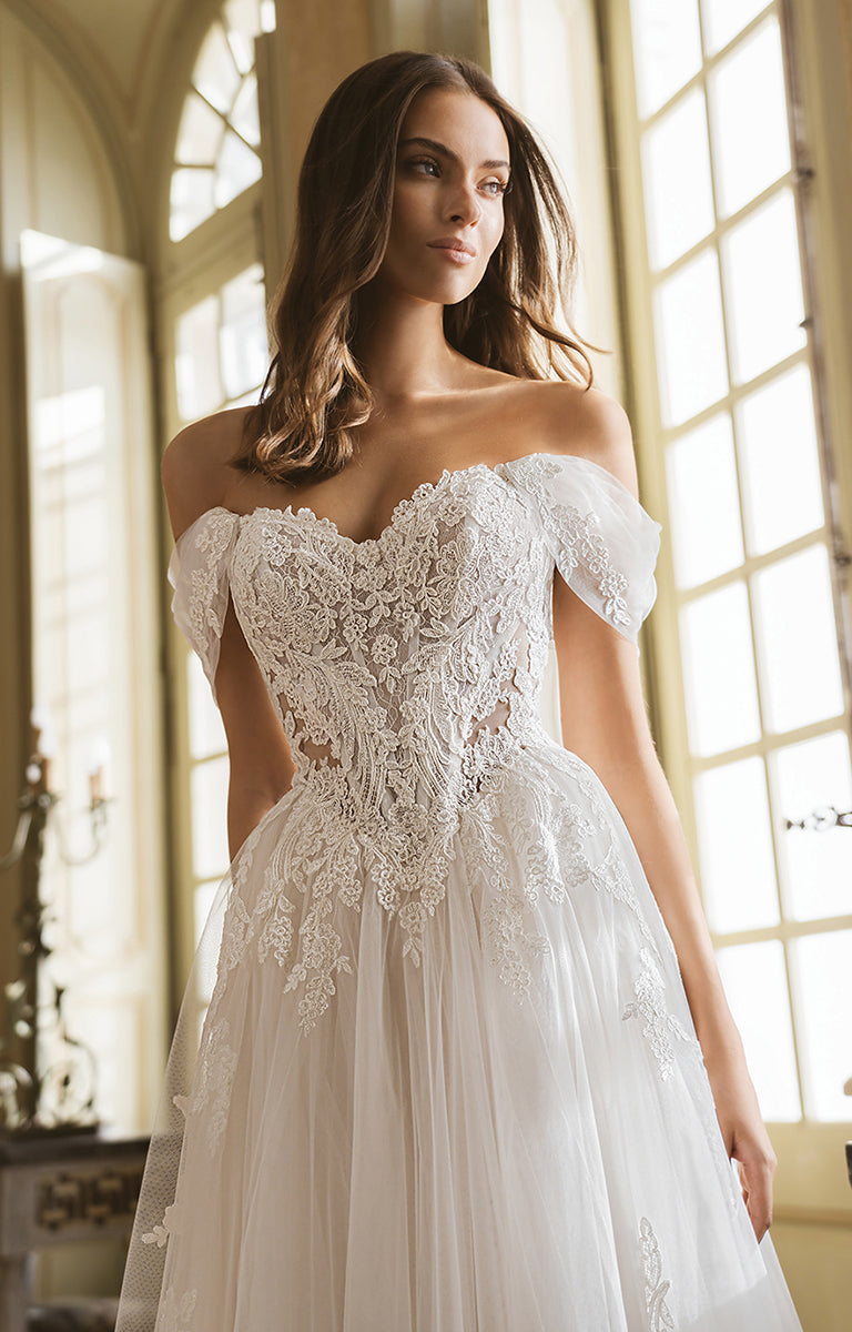 Woman wearing a white lace wedding dress in a bright room with large windows.