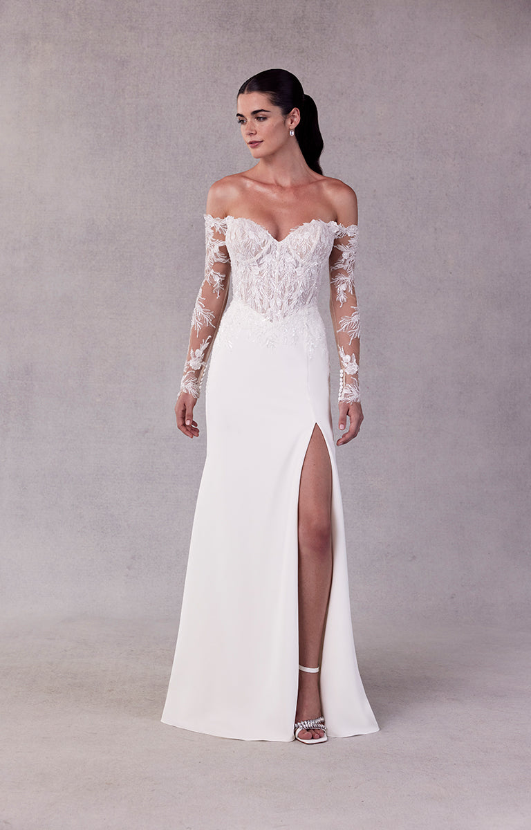 Woman wearing a white wedding dress with lace sleeves against a gray background