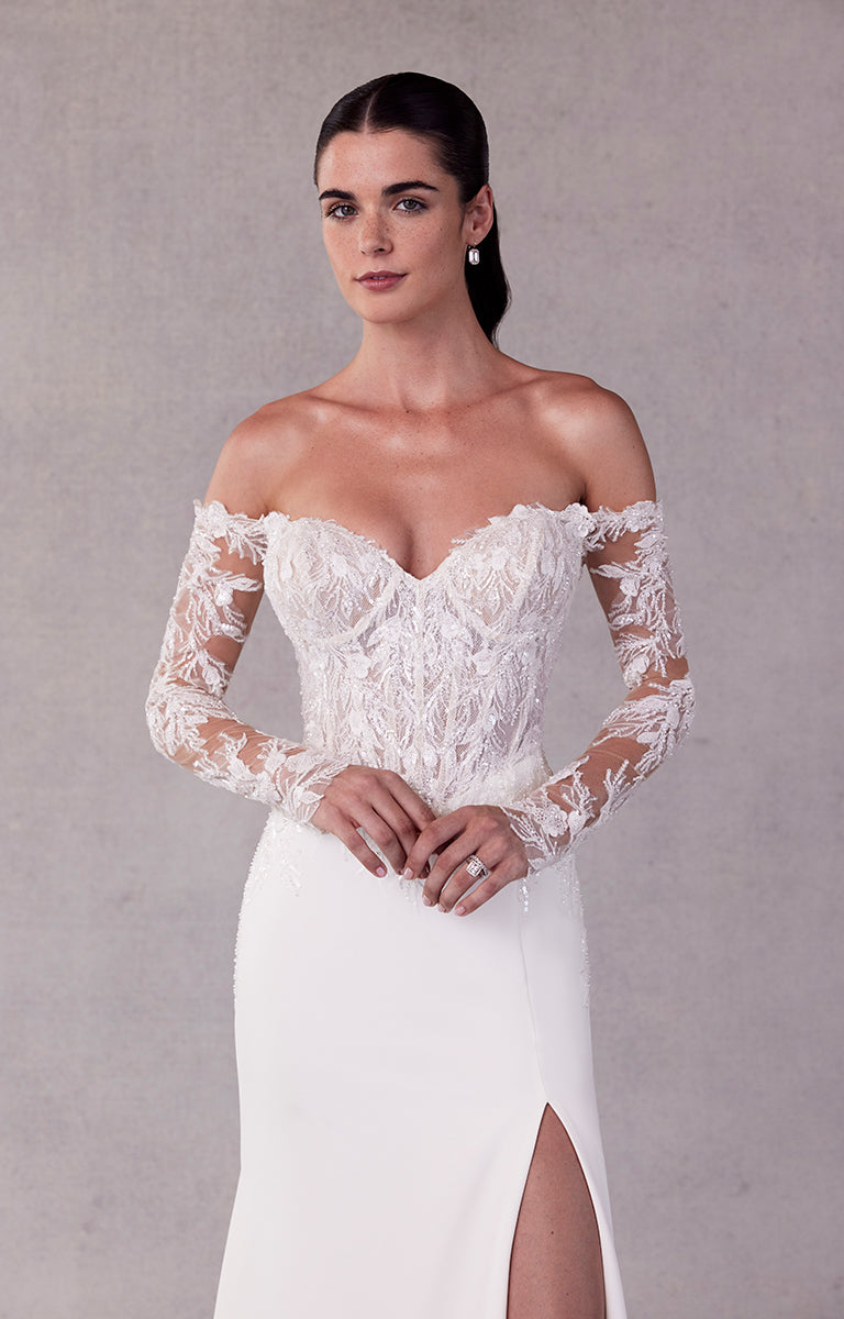 Woman wearing a white lace wedding dress with long sleeves against a gray background