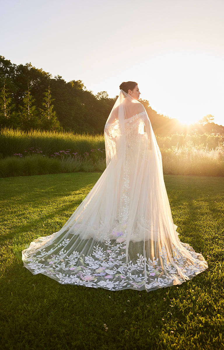 Woman in a white lace wedding dress standing in a grassy field with sunset lighting.