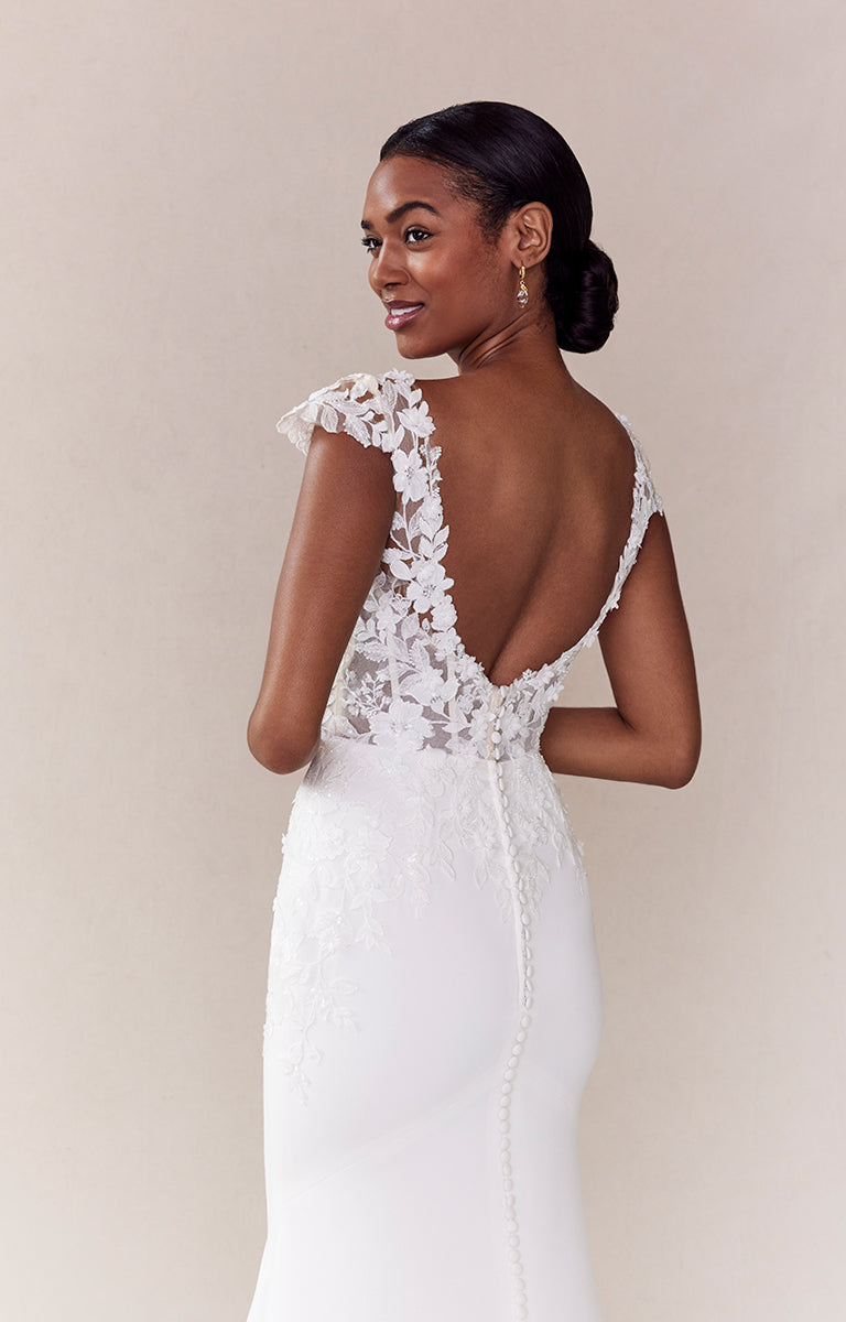 Woman wearing a white lace wedding dress with a low back on a beige background