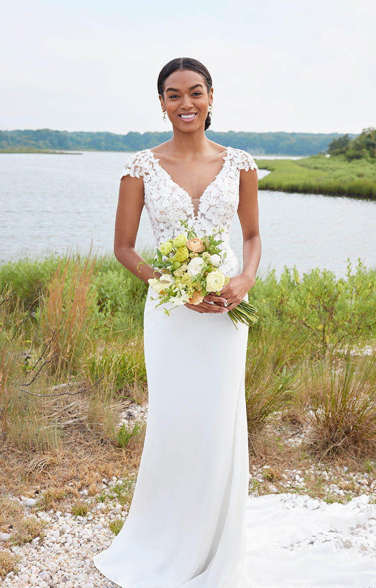 Bride in a white wedding dress holding a bouquet by a body of water.