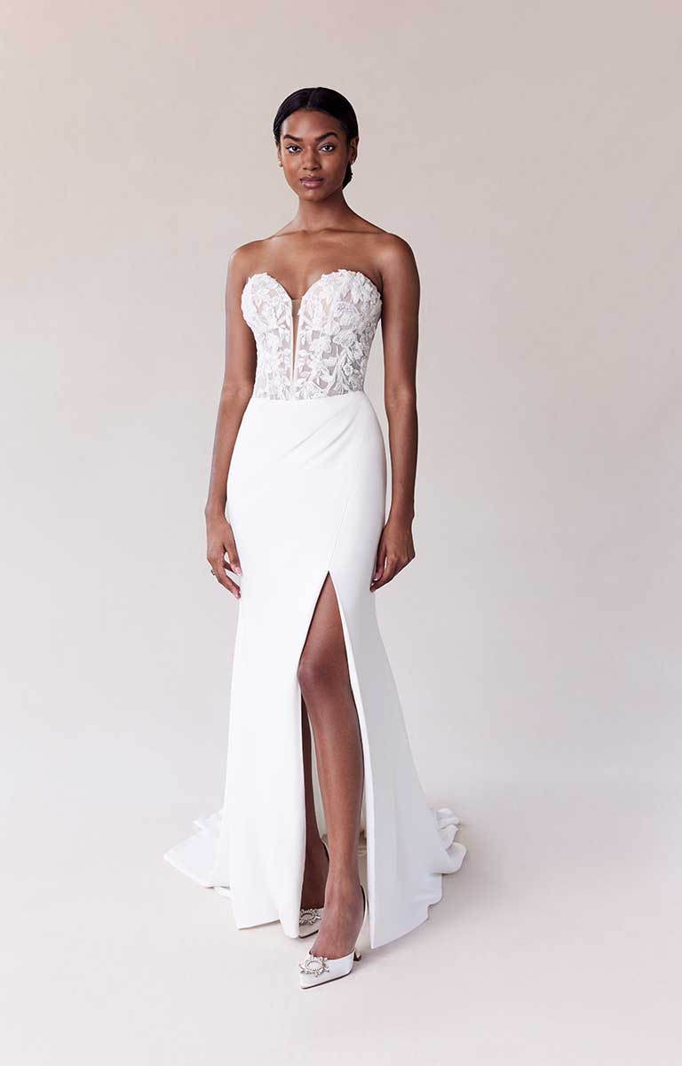 Woman wearing a white strapless gown with floral lace top on a plain background