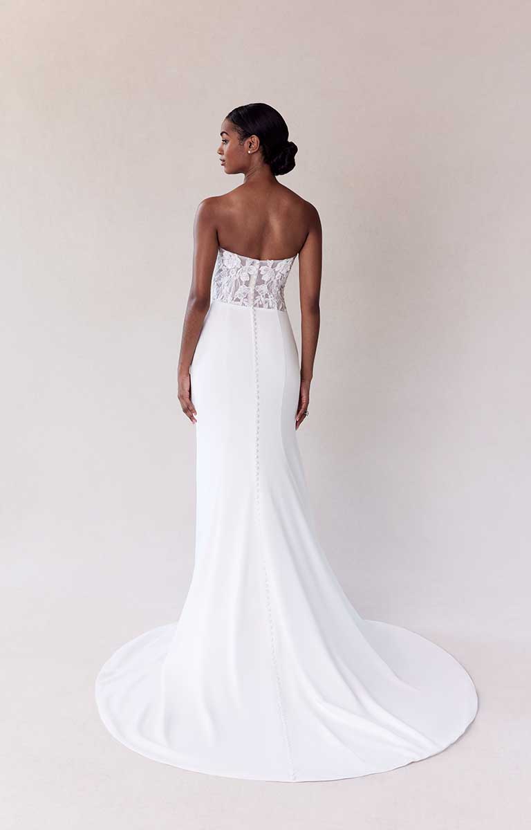 Woman wearing a white strapless wedding dress with lace detailing on a plain background
