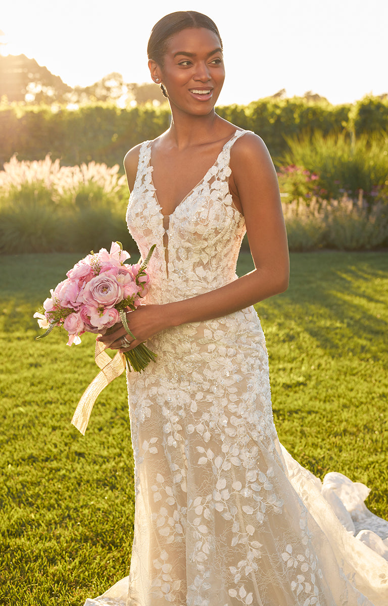 Woman in a lace wedding dress holding a bouquet of pink flowers in a grassy outdoor setting.