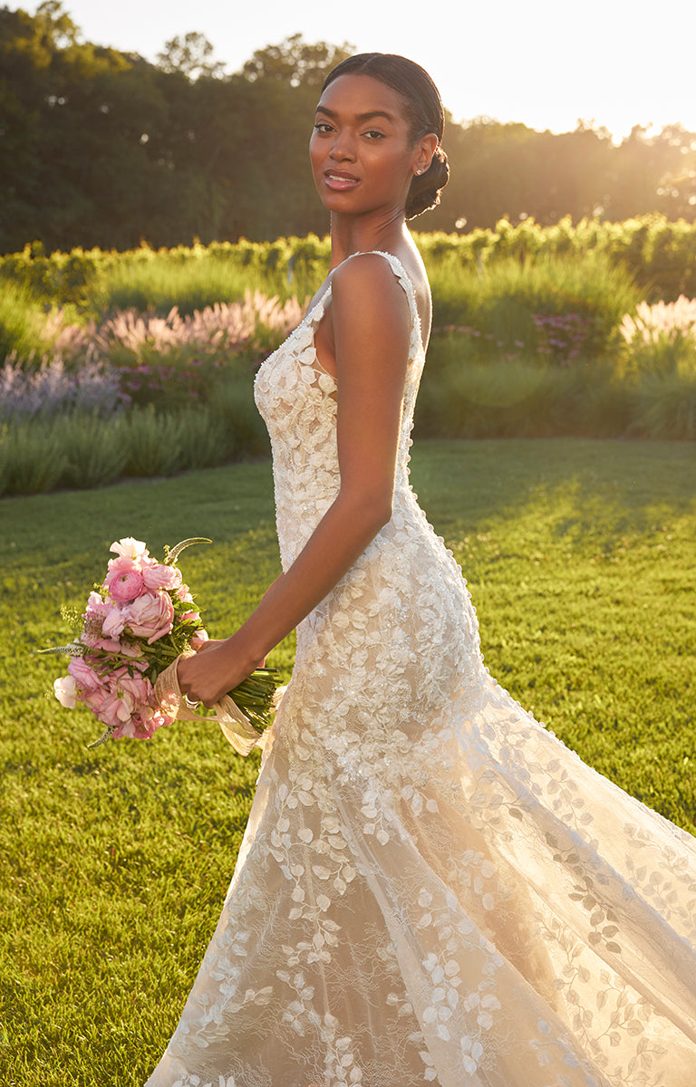 Woman in a white wedding dress holding a bouquet of flowers in a grassy field.