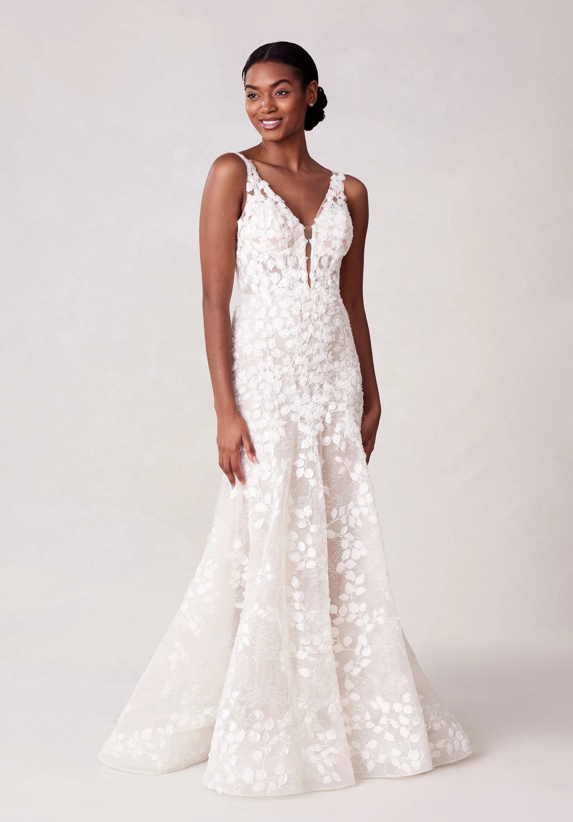 Woman wearing a white floral wedding dress against a plain background