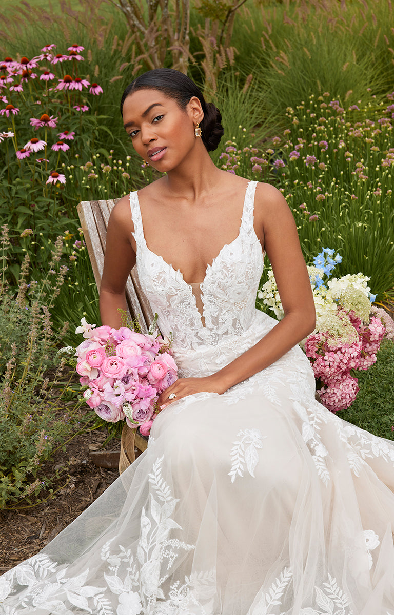 Woman in a white wedding dress holding pink flowers in a garden setting