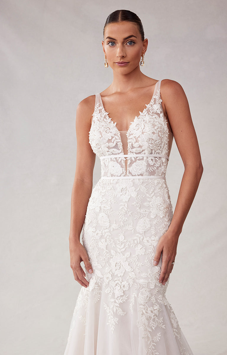 Woman wearing a white lace wedding dress against a plain background