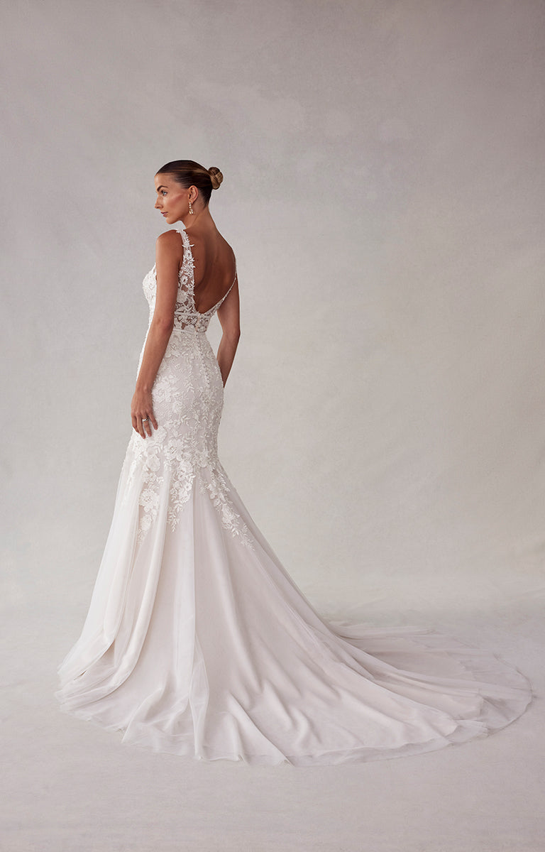 Woman wearing a white lace wedding dress against a plain background