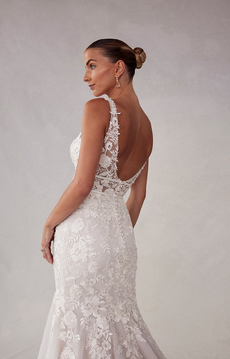 Woman wearing a white lace wedding dress with a low back on a plain background