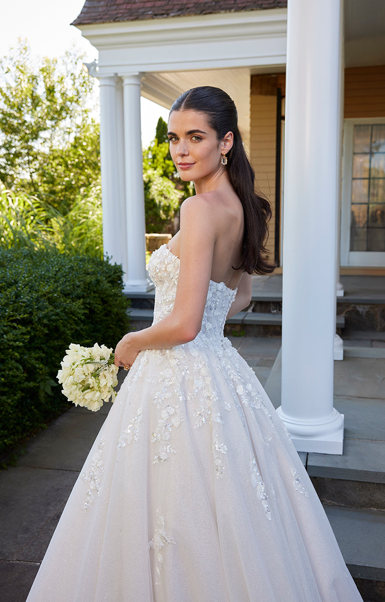 Woman in a strapless wedding dress holding a bouquet on a porch.