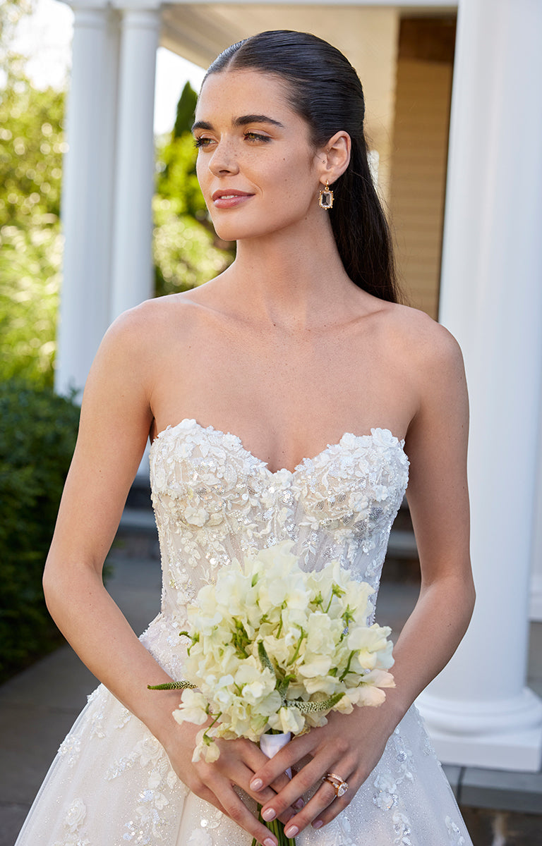 Woman in a white wedding dress holding flowers outdoors.