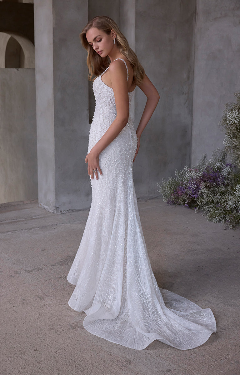 Woman in a white lace wedding dress standing in an outdoor setting with flowers.