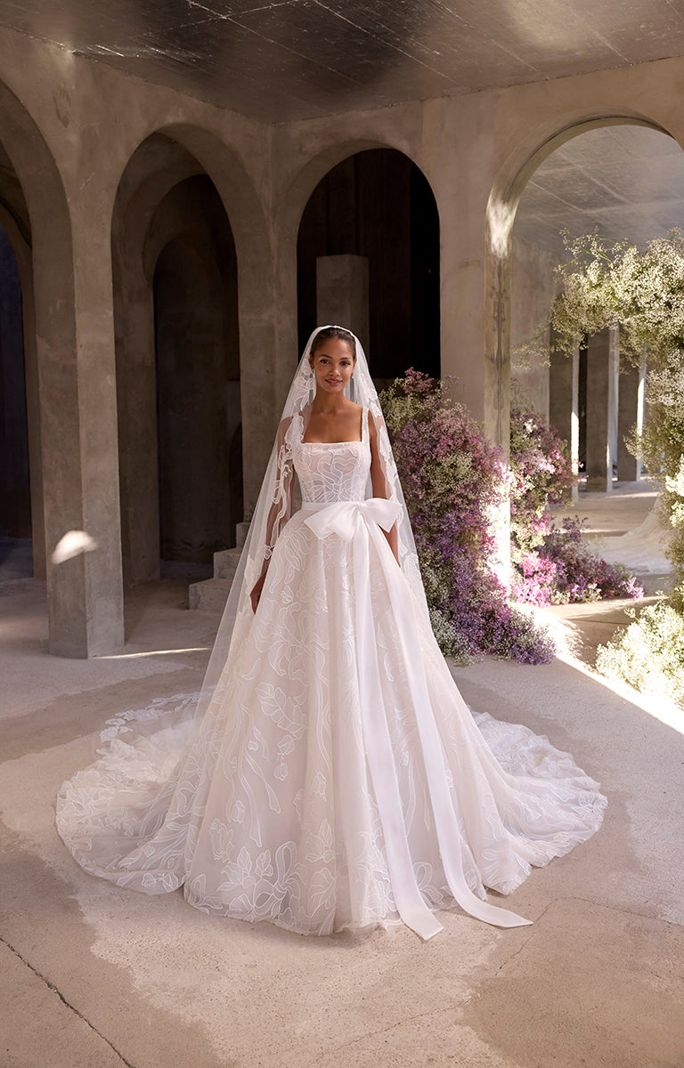Bride in a white wedding dress standing in an outdoor setting with arches and flowers.