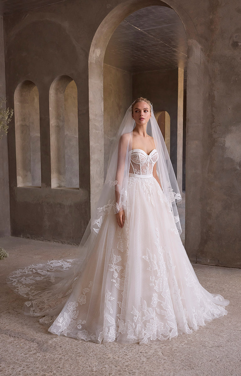 Woman in a white wedding dress standing in an archway with a long train.