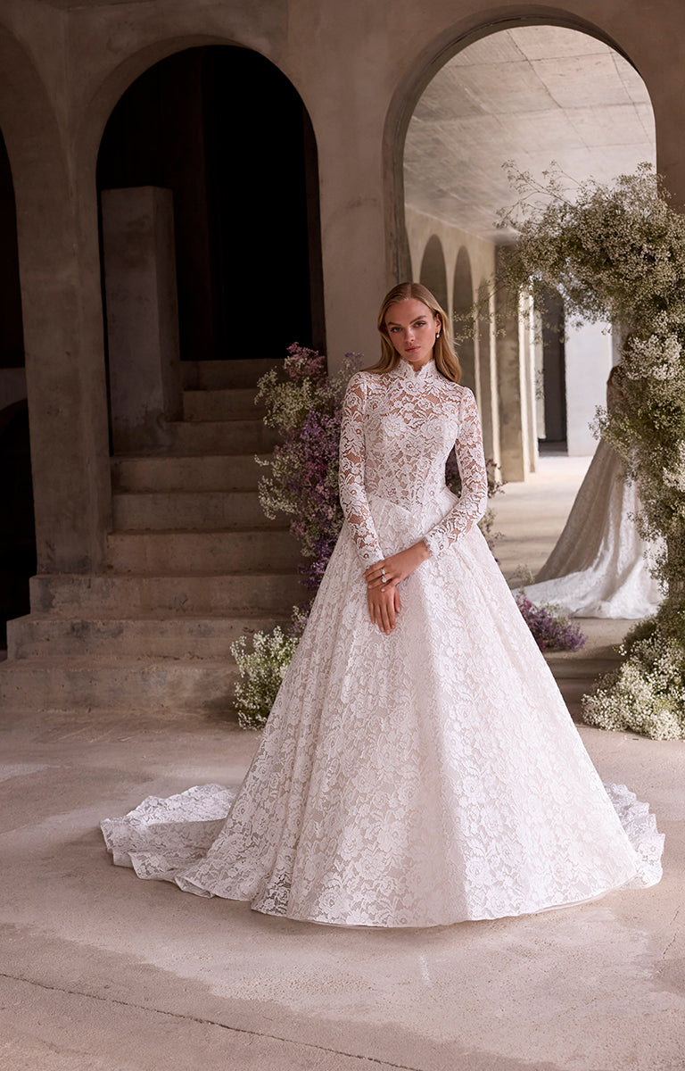 Woman in a white lace wedding dress standing in an elegant outdoor setting with arches and floral decorations.