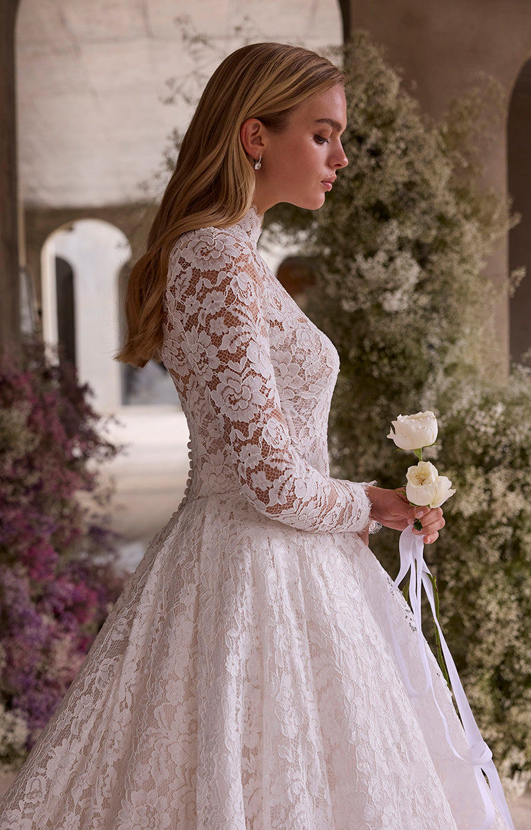 Woman in a lace wedding dress holding flowers in an outdoor setting