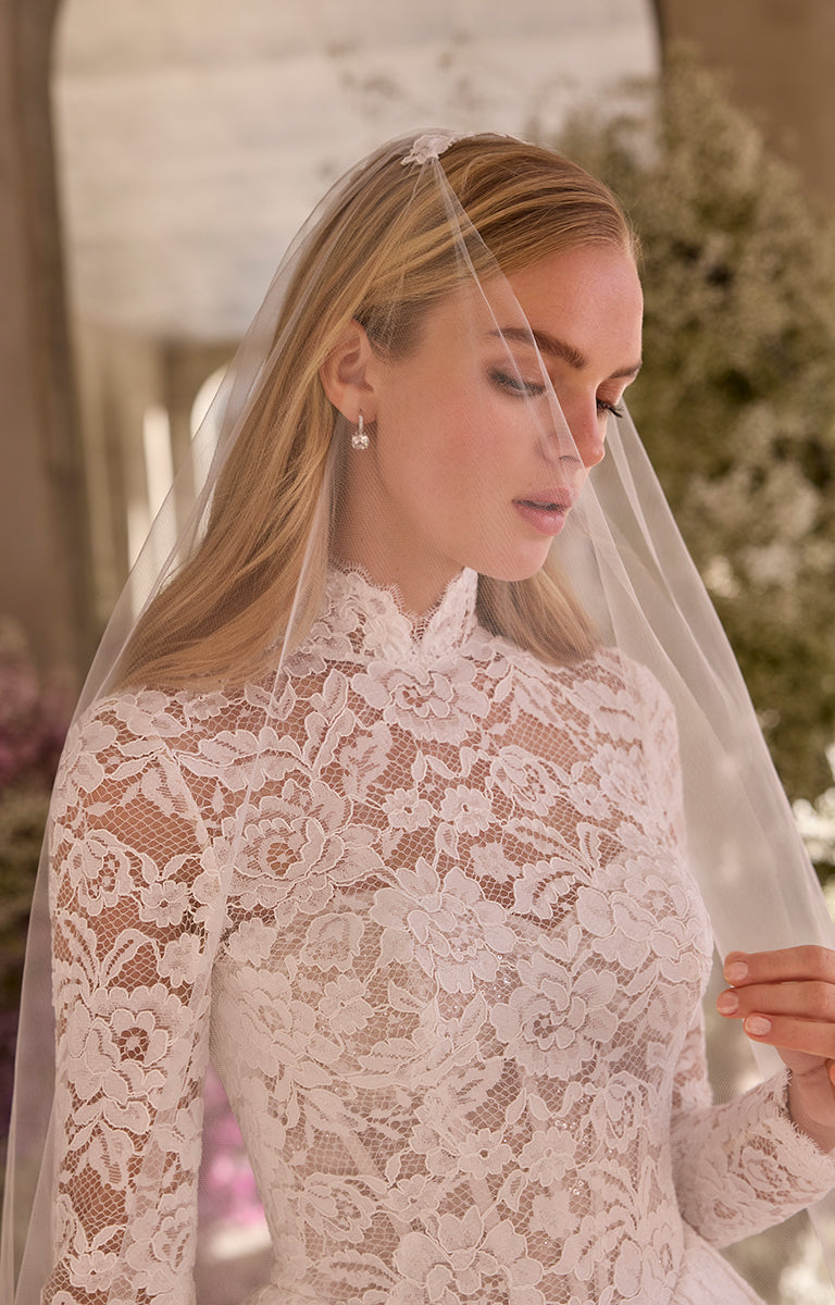 Bride wearing a lace wedding dress with a veil, standing outdoors.